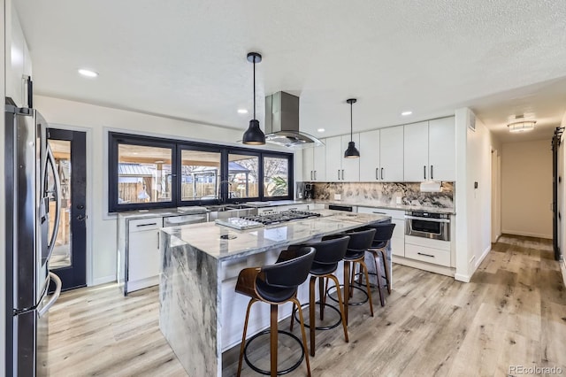 kitchen featuring island range hood, a center island, stainless steel appliances, light wood-type flooring, and backsplash