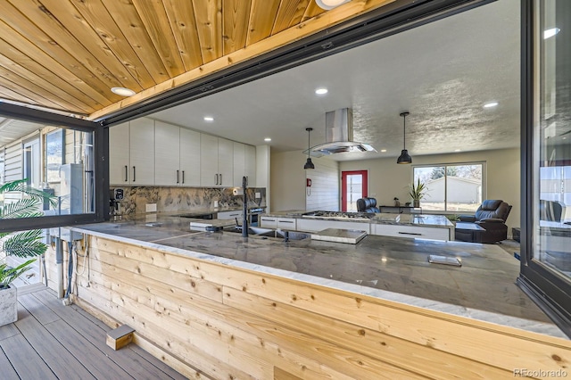 kitchen with island range hood, stainless steel gas cooktop, wood finished floors, white cabinets, and tasteful backsplash