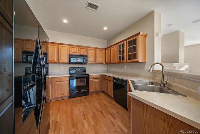kitchen featuring light countertops, visible vents, a sink, black appliances, and light wood-style flooring