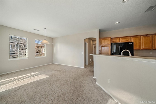 kitchen with visible vents, light carpet, arched walkways, brown cabinetry, and black fridge