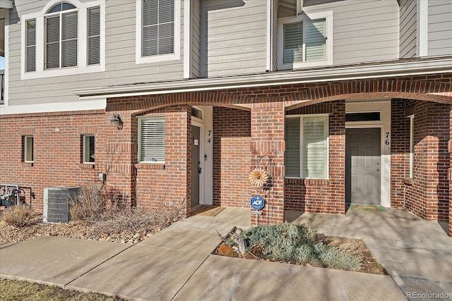 property entrance with central AC unit, brick siding, and covered porch