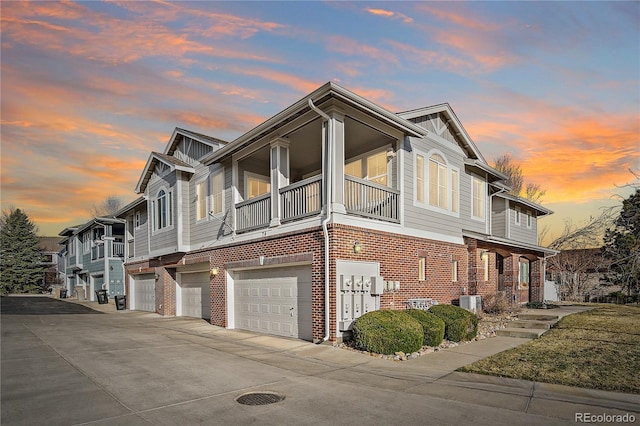 view of side of home featuring an attached garage, brick siding, driveway, and a balcony