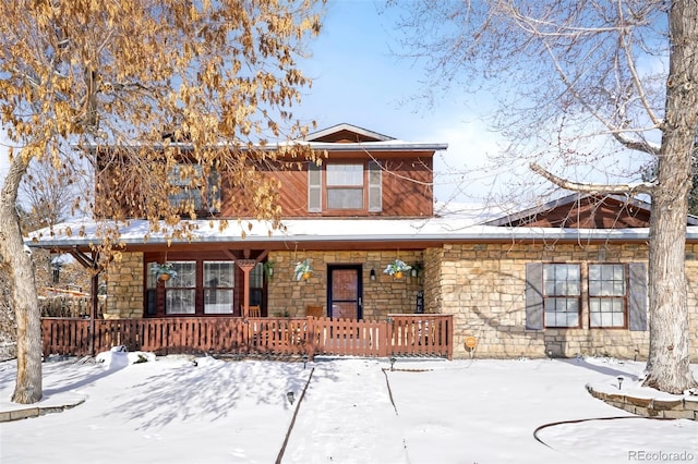 snow covered back of property with a porch and stone siding