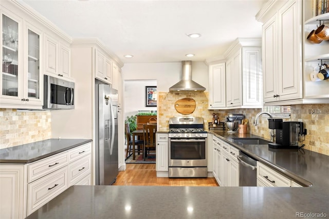 kitchen with stainless steel appliances, wall chimney range hood, dark countertops, and glass insert cabinets