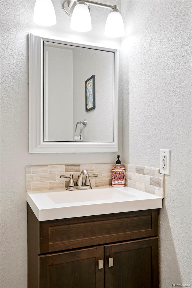 bathroom featuring a textured wall, decorative backsplash, and vanity