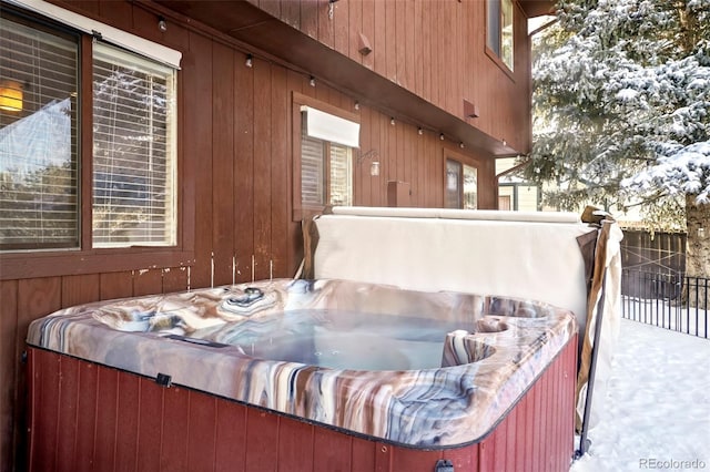 view of snowy exterior featuring fence and a hot tub