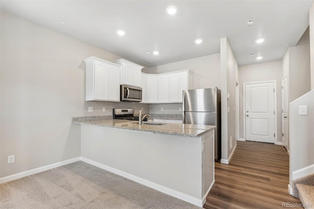 kitchen featuring light stone countertops, dark wood-type flooring, stainless steel appliances, kitchen peninsula, and white cabinets