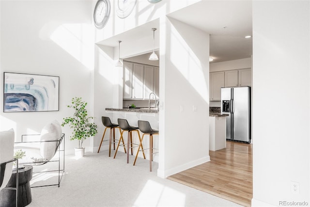 kitchen with sink, gray cabinetry, decorative light fixtures, stainless steel fridge with ice dispenser, and a kitchen breakfast bar