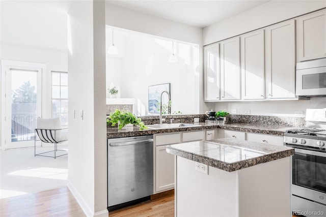 kitchen with sink, white cabinetry, hanging light fixtures, appliances with stainless steel finishes, and light hardwood / wood-style floors