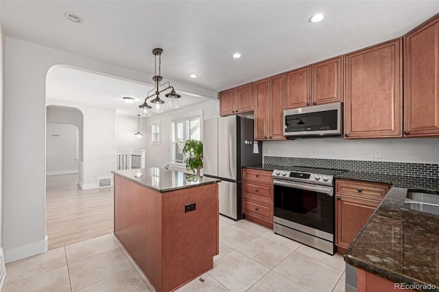 kitchen with pendant lighting, light tile patterned floors, appliances with stainless steel finishes, a kitchen island, and dark stone counters