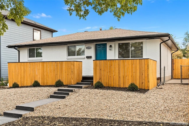 view of front of house featuring brick siding, fence, and roof with shingles