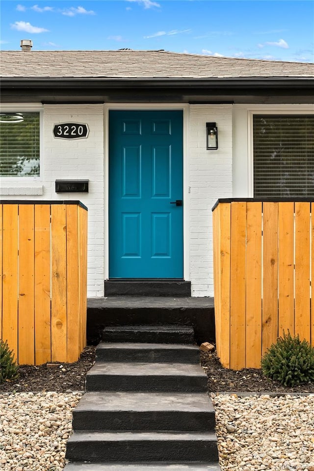 view of exterior entry with a shingled roof and brick siding