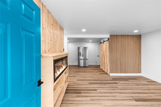 kitchen with recessed lighting, stainless steel fridge with ice dispenser, a barn door, light wood-style floors, and baseboards