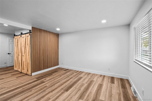 spare room with a barn door, wood finished floors, and baseboards