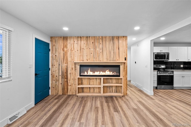 unfurnished living room with recessed lighting, visible vents, light wood-style flooring, a glass covered fireplace, and baseboards