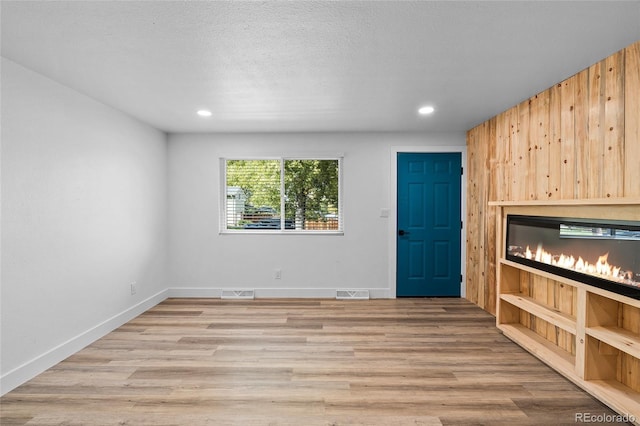 unfurnished living room with baseboards, light wood-style flooring, visible vents, and a textured ceiling