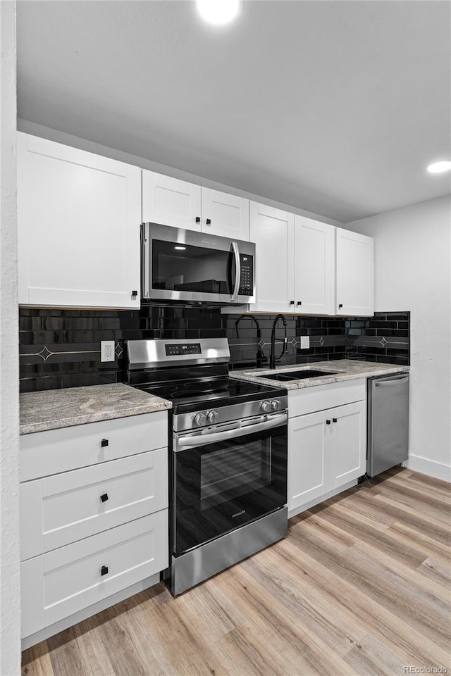 kitchen featuring appliances with stainless steel finishes, a sink, white cabinetry, and light wood-style floors