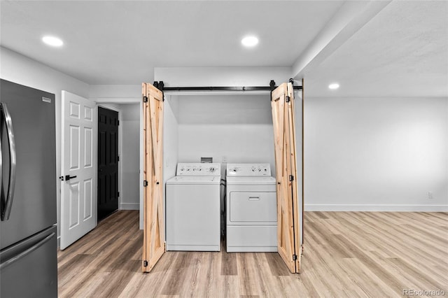 laundry area with laundry area, a barn door, light wood-style flooring, and washer and dryer