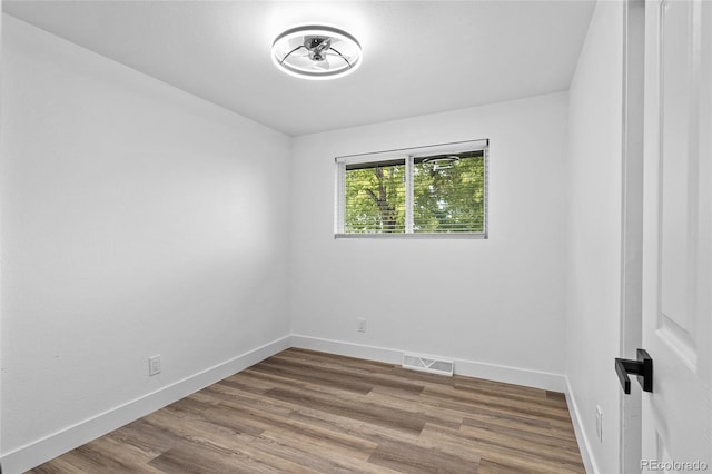 empty room featuring wood finished floors, visible vents, and baseboards