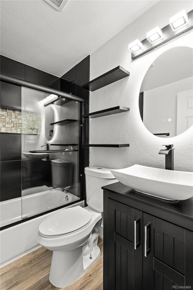 full bathroom featuring a textured ceiling, a textured wall, wood finished floors, and enclosed tub / shower combo