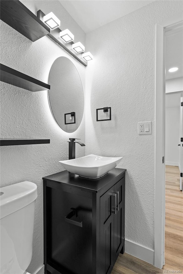 bathroom featuring a textured wall, toilet, vanity, wood finished floors, and baseboards