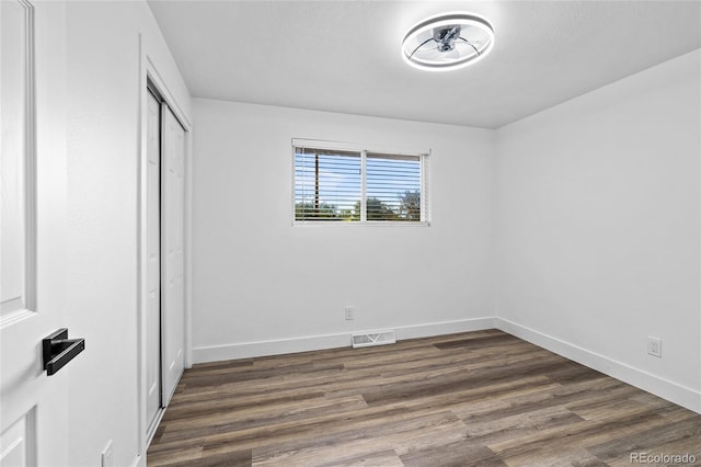 unfurnished bedroom with dark wood-style floors, a closet, visible vents, and baseboards