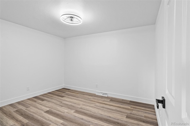 unfurnished room featuring baseboards, visible vents, and wood finished floors