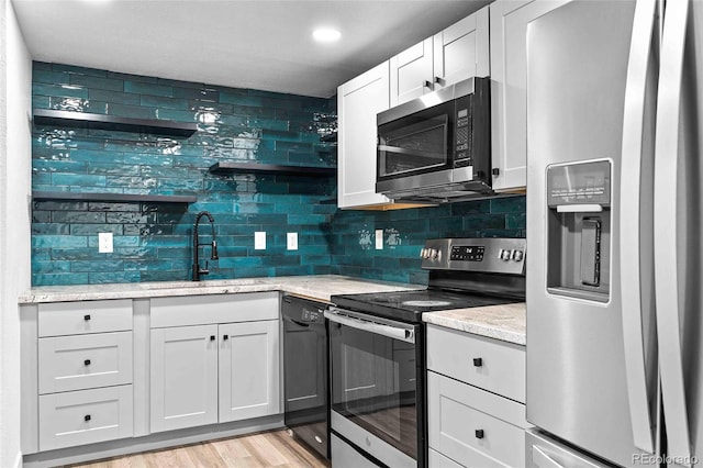 kitchen featuring tasteful backsplash, white cabinets, light wood-style flooring, stainless steel appliances, and a sink