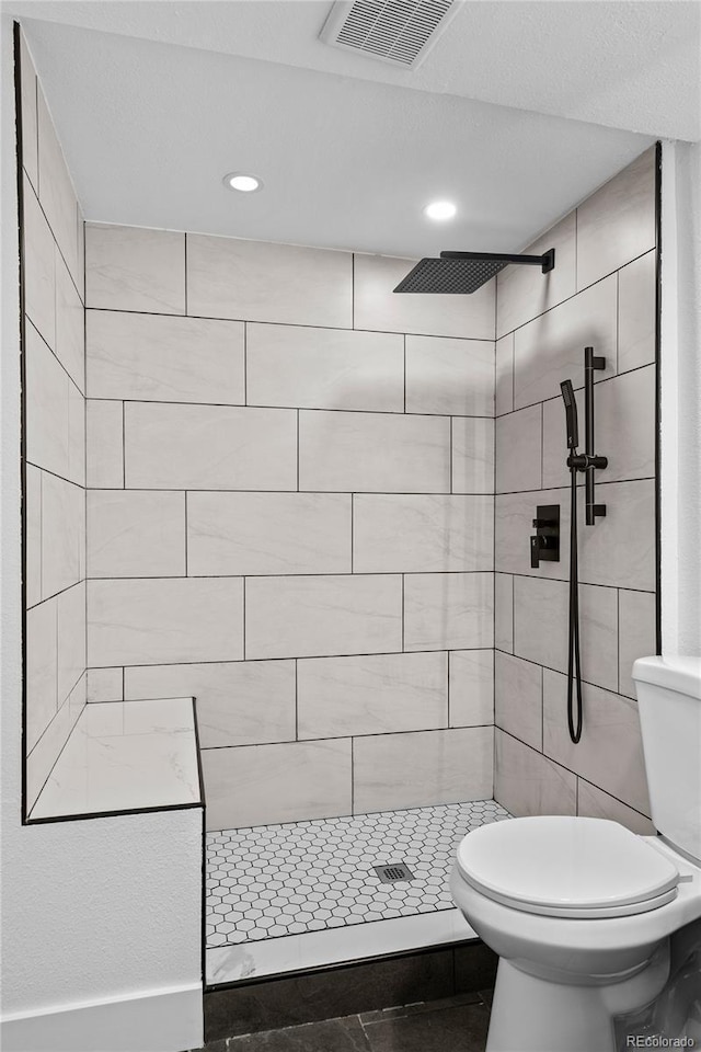 bathroom featuring toilet, visible vents, tiled shower, and recessed lighting