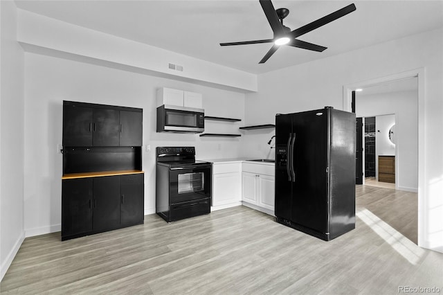 kitchen featuring light countertops, white cabinetry, a sink, light wood-type flooring, and black appliances