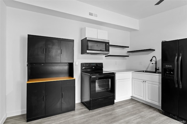 kitchen with a sink, visible vents, white cabinetry, light countertops, and black appliances