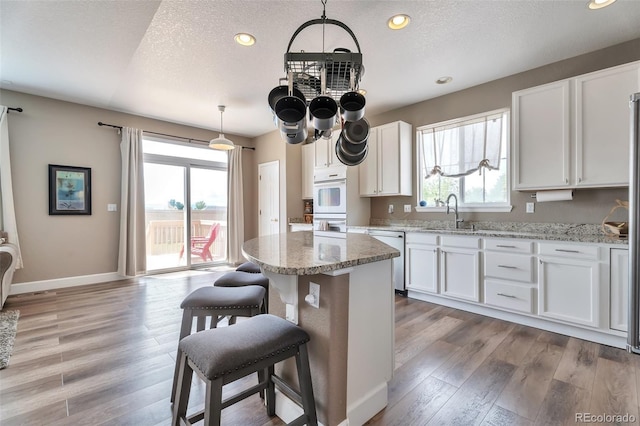 10695 Wynspire Rd, Highlands Ranch, CO 80130 - kitchen with a sink, dishwasher, a breakfast bar, white cabinetry, and light wood finished floors