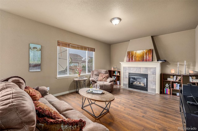 living room with wood-type flooring, a textured ceiling, and a tile fireplace