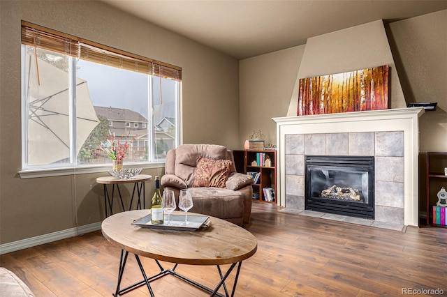 living area with wood-type flooring and a tiled fireplace