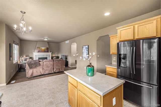 kitchen with a fireplace, a kitchen island, decorative light fixtures, stainless steel fridge with ice dispenser, and a chandelier