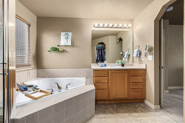 bathroom with vanity, a textured ceiling, tile patterned flooring, and tiled bath