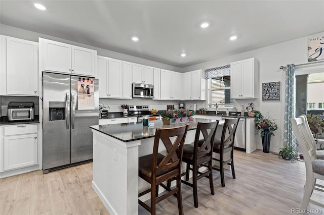 kitchen featuring white cabinetry, appliances with stainless steel finishes, light wood-type flooring, a breakfast bar, and a center island