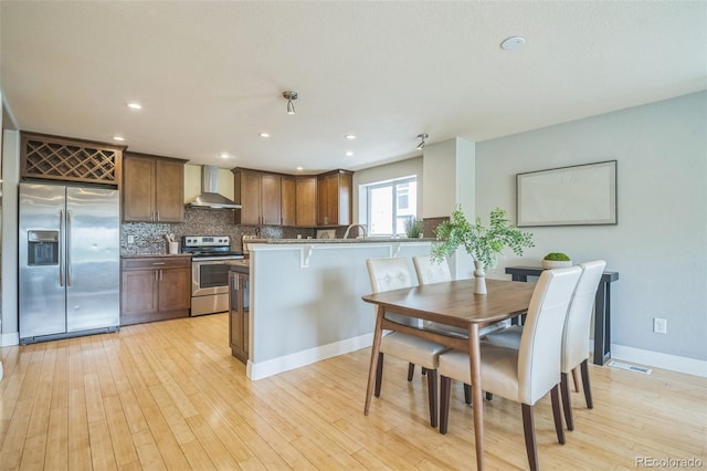 2539 N York St, Denver, CO 80205 - kitchen with stainless steel appliances, wall chimney exhaust hood, light wood-style flooring, backsplash, and recessed lighting