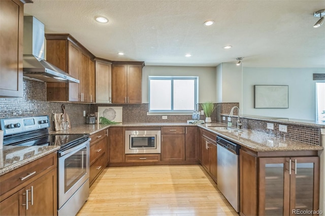 2539 N York St, Denver, CO 80205 - kitchen with stainless steel appliances, a sink, wall chimney range hood, a peninsula, and light wood-style flooring