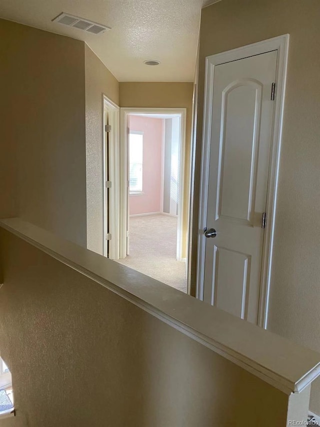 hall featuring carpet, visible vents, a textured wall, and a textured ceiling