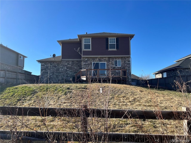 rear view of house featuring fence, stone siding, and a wooden deck