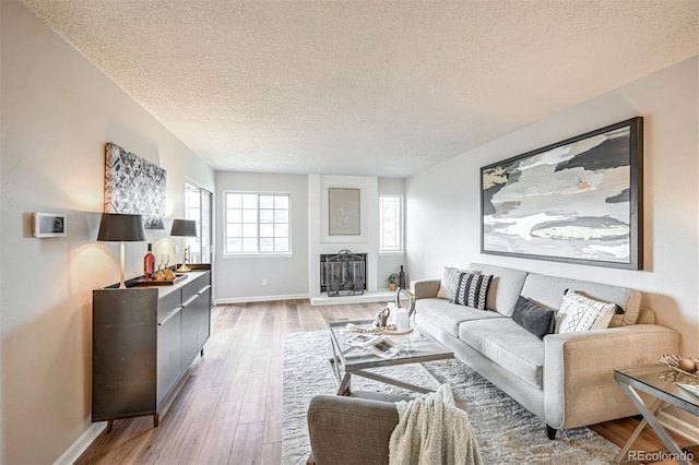 1470 S Quebec Way Unit 62, Denver, CO 80231 - living room with a textured ceiling, light wood-type flooring, baseboards, and a fireplace with raised hearth