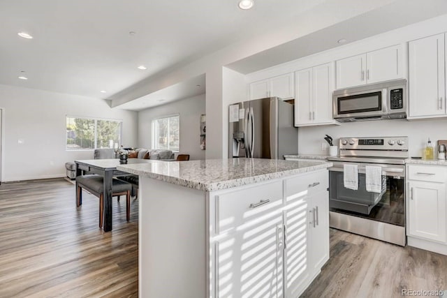 kitchen featuring light stone countertops, a center island, stainless steel appliances, light hardwood / wood-style flooring, and white cabinets