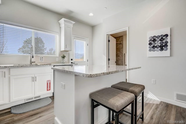 kitchen featuring light stone countertops, a breakfast bar, white cabinets, and sink