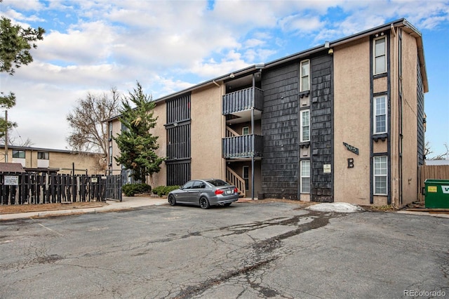 view of building exterior with uncovered parking, central AC, and fence