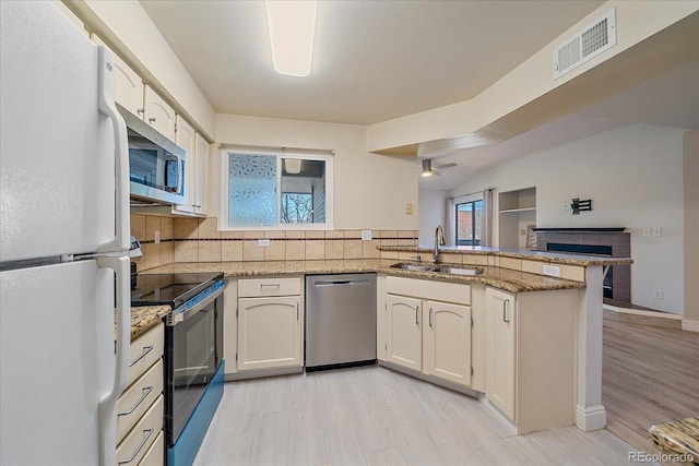 kitchen featuring ceiling fan, kitchen peninsula, decorative backsplash, sink, and appliances with stainless steel finishes