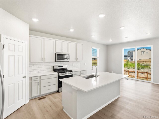 17487 E 89th Way, Commerce City, CO 80022 - kitchen featuring appliances with stainless steel finishes, a sink, light wood-style flooring, decorative backsplash, and a center island with sink
