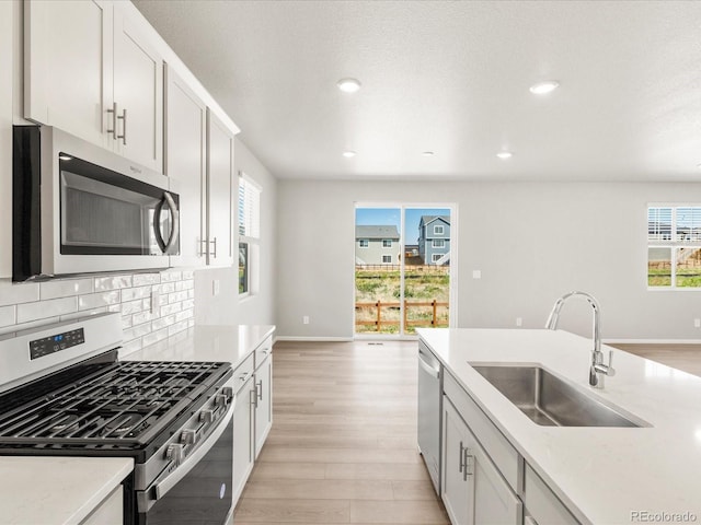 17487 E 89th Way, Commerce City, CO 80022 - kitchen featuring appliances with stainless steel finishes, a sink, light wood finished floors, backsplash, and baseboards
