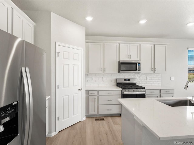 17487 E 89th Way, Commerce City, CO 80022 - kitchen featuring stainless steel appliances, a sink, light wood-style floors, backsplash, and white cabinetry