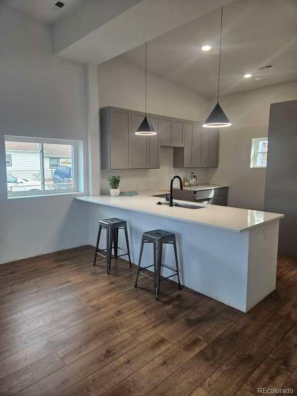 kitchen with dark wood finished floors, gray cabinets, a kitchen bar, and a sink